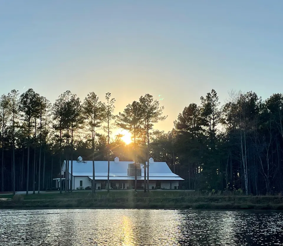 The white timber-frame barn across the farm lake at sunset, framed by pines